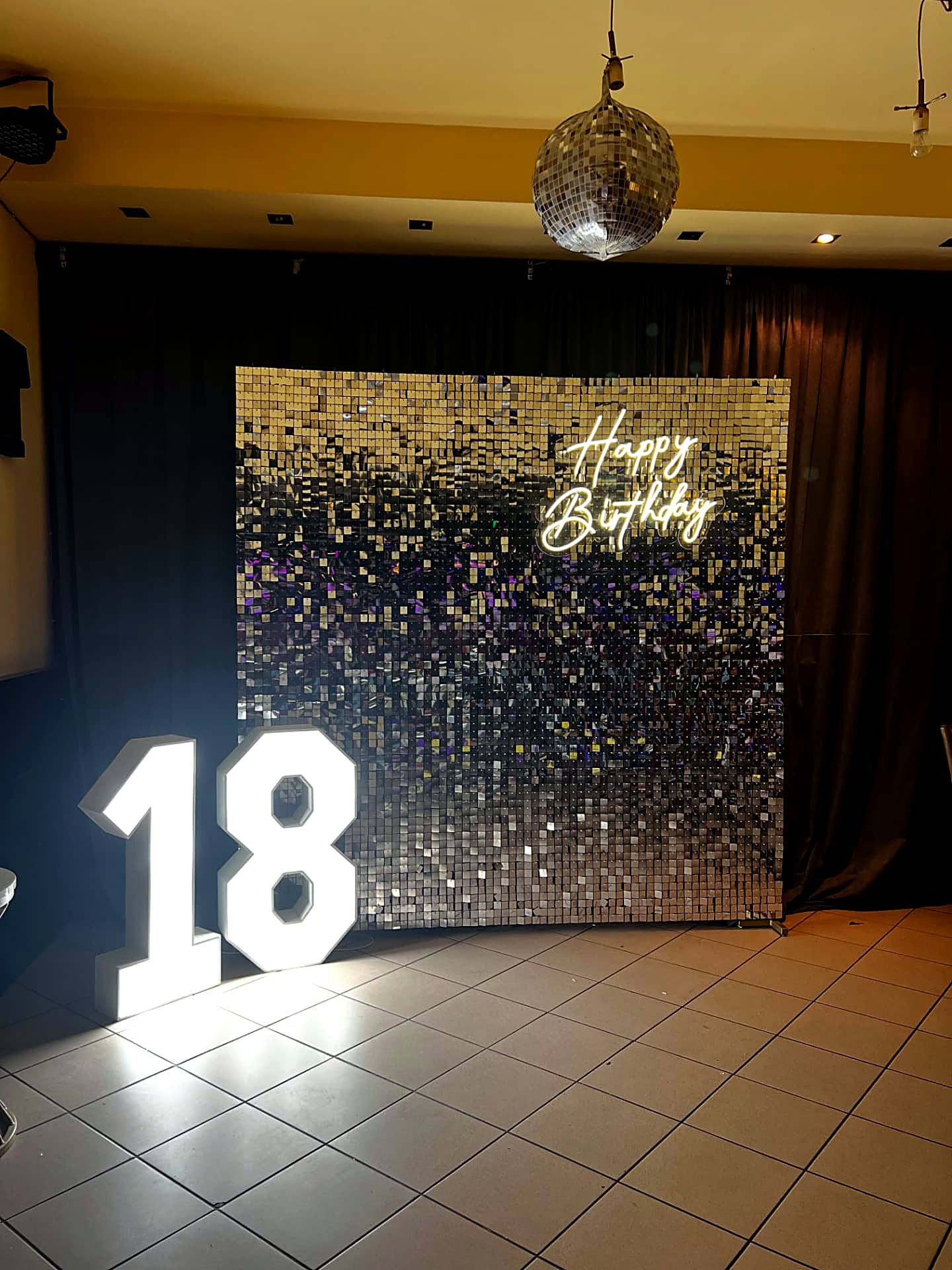 Zlatno-srebrni shimmer zid sa neonom Happy Birthday i svetlećim brojem 18